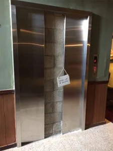 A closed metallic elevator with a 'Sorry - out of service' sign hanging on it, set in a commercial space with green walls and