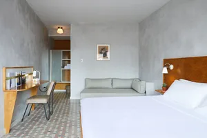 Modern minimalist bedroom featuring concrete walls and floor, a white bed, and a grey couch.