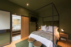 A modern, minimalist bedroom featuring a four-poster bed, wooden flooring, and green walls.