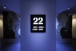 A minimalist hotel room directory with numbered rooms and directional signs, mounted on a metal panel.