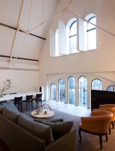 Modern minimalist living room with white walls, arched windows, wooden furniture, and a grey sofa.