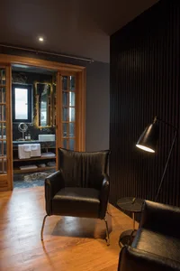 A minimalist living room featuring wooden flooring, black leather armchair, and metallic floor lamp.