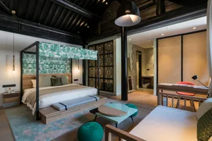 Modern bedroom in a converted barn with wooden beams, a green and white bed canopy, and a minimalist design