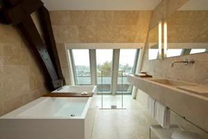 Modern bathroom with a white freestanding bathtub, a large marble sink vanity, and a large window providing a city view.