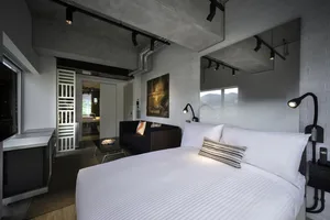 Modern bedroom with minimalist design, featuring concrete walls and white bedding.