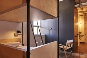 A modern bunk bed with a wooden frame and ladder, featuring a bed with a pillow on the lower bunk and a chair in the foregrou