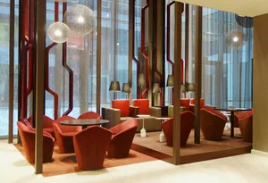 Modern hotel lobby featuring red fabric furniture, concrete and glass surfaces, and steel accents.