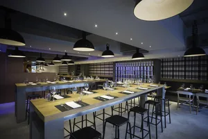 A sleek, industrial-themed restaurant interior with high tables, chairs, and pendant lights.