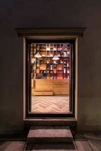 A retail storefront with wooden shelves filled with candles and decorative items, viewed through a window with a chevron-patt