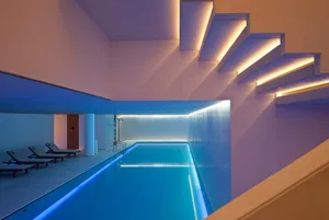 A modern indoor swimming pool with glass walls and illuminated steps.