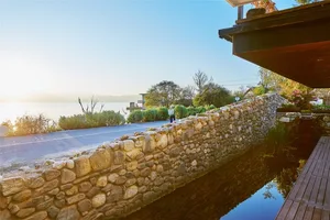 A stone wall along a water body, with a wooden deck and a building in the background.