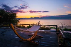 An empty hammock against a serene sunset backdrop on a wooden veranda overlooking the sea and mountains.