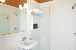 A modern minimalist bathroom featuring white terrazzo tiles, a sleek glass shower enclosure, and a clean white sink.