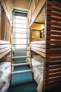 A hostel room with wooden bunk beds, metal ladder, and fabric curtains.