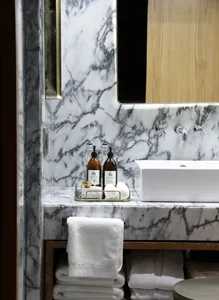 A modern bathroom with marble accents, a sink, and neatly stacked white towels.