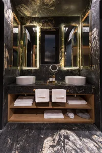 A modern marble bathroom with two sinks, mirrors, towels, and a vanity.