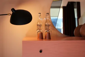 A modern nightstand with a clear glass bottle and a sleek, black wall lamp. The scene features contemporary lighting and mini