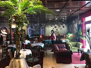 Modern restaurant interior with green leather chairs, silk palm plants, and other decorative elements.