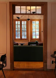 A view into a wooden living room, featuring a green sofa and a window with wooden frames.