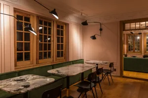 Interior of a modern cafe with marble tables, green upholstered seating, and wooden floors.