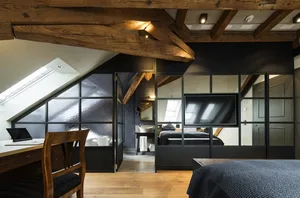 A modern, industrial-style bedroom featuring wooden beams on the ceiling and a large window.