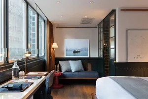 Industrial-style hotel room featuring modern furniture, wooden floors, and a large window.