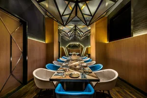 Long dining table with blue and white cushioned chairs in a modern industrial restaurant setting
