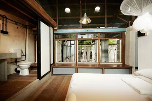 Minimalist bedroom with wood flooring and furnishings, featuring a bed and bathroom area.