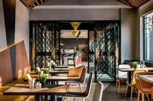 Modern cafe interior featuring metallic and glass panels, brick walls, and wooden tables.