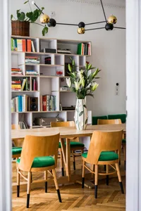 Modern dining room featuring wooden furniture, green upholstered chairs, and a white and green vase with white flowers.