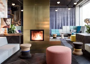 A modern hotel lounge with a fireplace, contemporary seating, and metallic, wooden, and concrete decor.