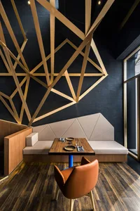Modern industrial restaurant booth with wood and concrete materials, featuring a geometric wall design and a single orange up