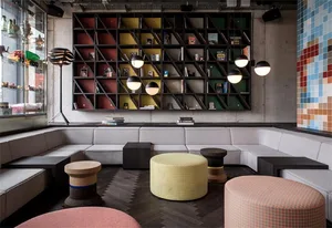 A modern lounge area with concrete walls, wooden seating, and fabric-covered stools.