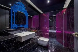 A modern marble bathroom with purple accents and a unique mirror frame.