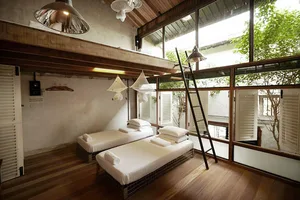 A minimalist bedroom with white bedding, wood floors, and large windows.