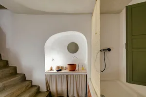 A minimalist bathroom with a plaster wall, an arched sink, a round mirror, and a glass shower enclosure.