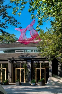 A modern metal sculpture depicting two rabbits in a garden setting.
