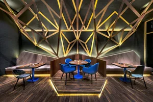 A modern restaurant dining room featuring geometric metal wall art, wooden seating, and warm lighting