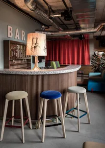 Bar area with industrial design elements, including metal stools and fabric seating, in a bar setting.