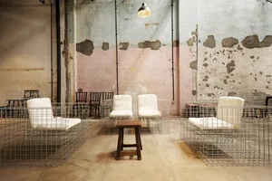 Industrial-style cafe space with metal wire cages enclosing cushioned chairs, wood stool, and exposed concrete and peeling pa