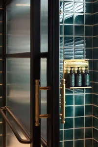 Industrial-style bathroom with green tiles, featuring a frosted glass shower door and brass handles.
