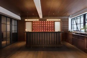 An industrial-style restaurant bar with a wooden counter, red lighting, and wooden walls