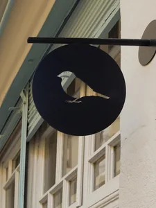 A round, black metal sign featuring the silhouette of a bird attached to a building.