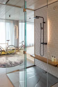 A minimalist bathroom with glass shower enclosure, wooden shelf, and white ceramic tiles.