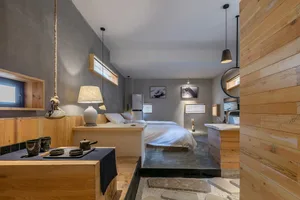 A minimalist bedroom featuring wooden and concrete elements, with a single bed, hanging lamps, and minimalist furnishings.