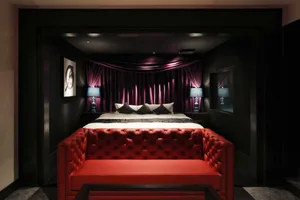 Modern minimalist bedroom featuring a red sofa, blue lamps, and a backlit curtain.