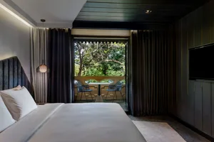 Clean, well-designed minimalist bedroom with grey curtains, a bed with a grey headboard, a small table with two chairs on a b