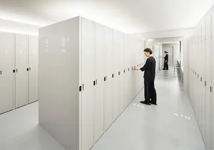 A minimalist office space featuring metal lockers with numbered labels on a white floor and walls.