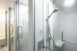 A modern bathroom with glass shower enclosures, metal hardware, and white tiled walls.