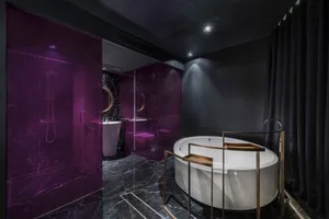 A modern bathroom featuring a white oval bathtub, dark marble tiles, and purple glass walls.